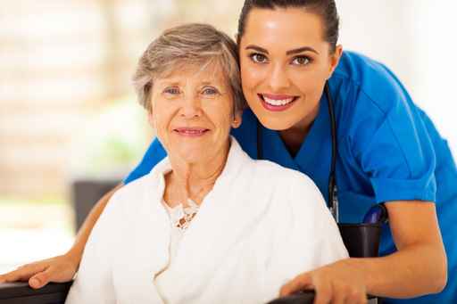 Caregiver stands behind elderly woman in wheelchair