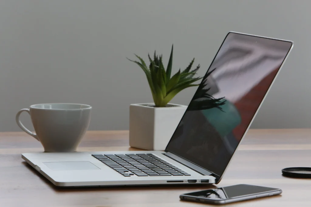 Laptop sitting on table with a cup and iphone next to it