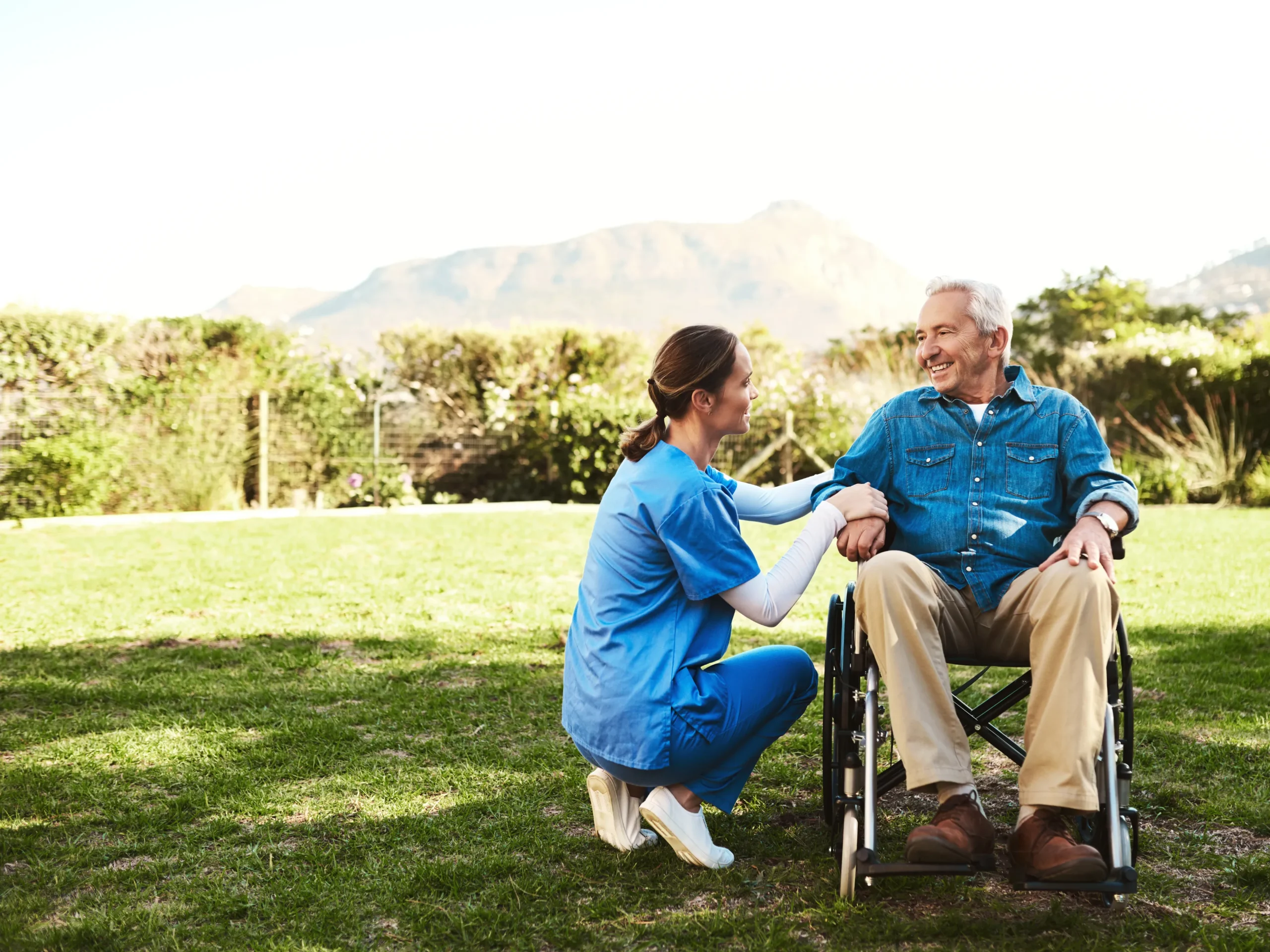 nurse and elderly man in wheel chair smiling outside