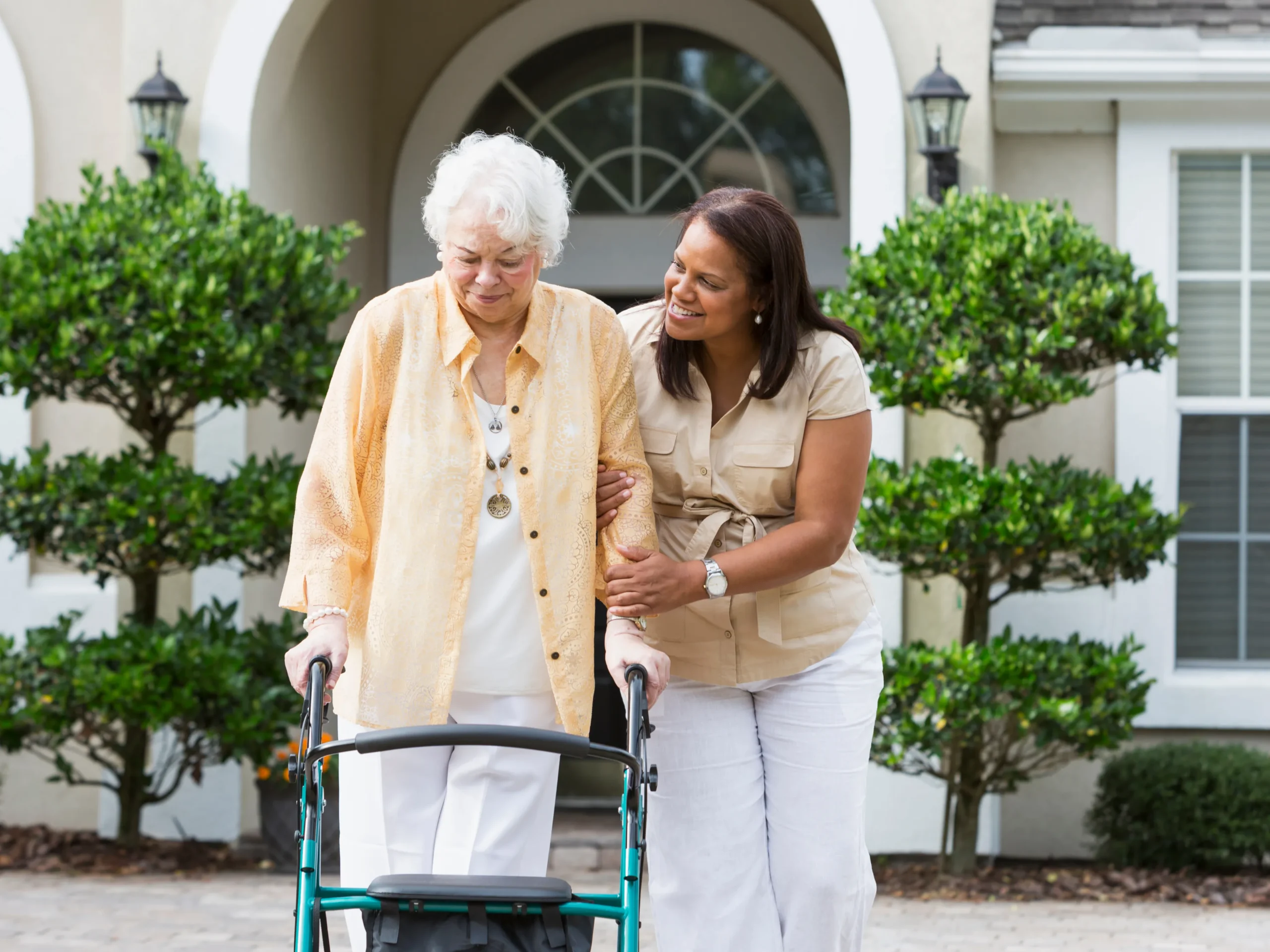 woman helping elderly woman walk using a walker