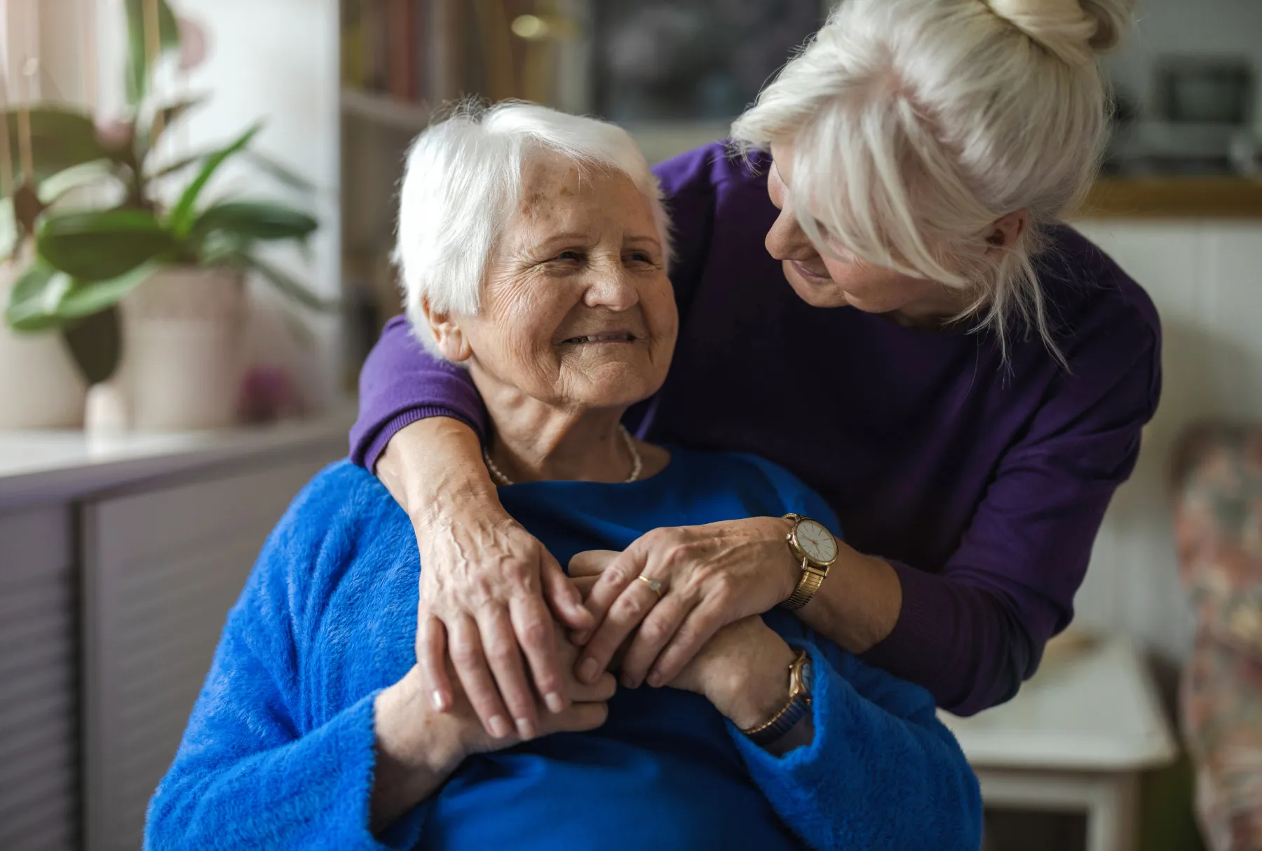 woman leaning over shoulder of smiling elderly woman